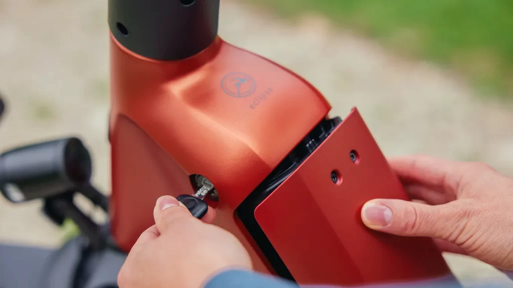 A person holding a red e bike's key and taking out its battery