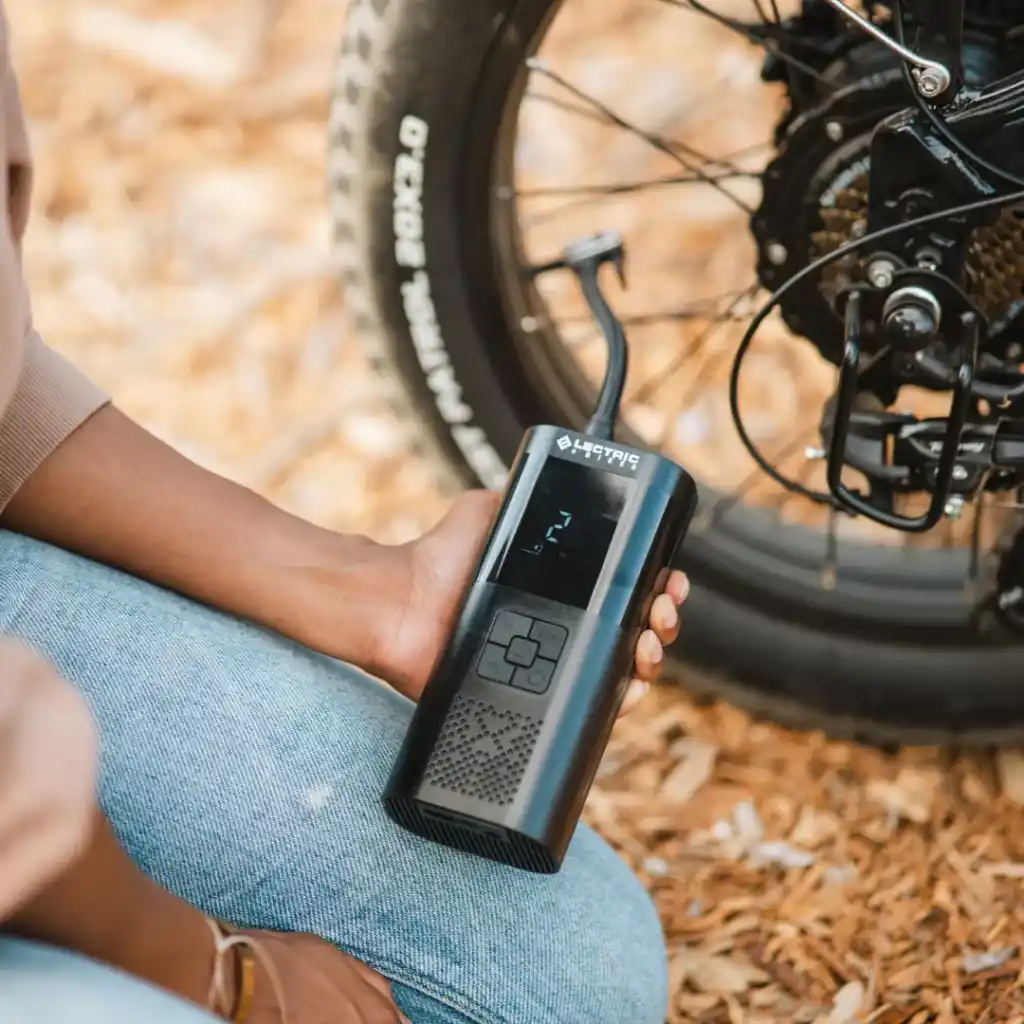 A person holding an electric air pump next to a bike tyre