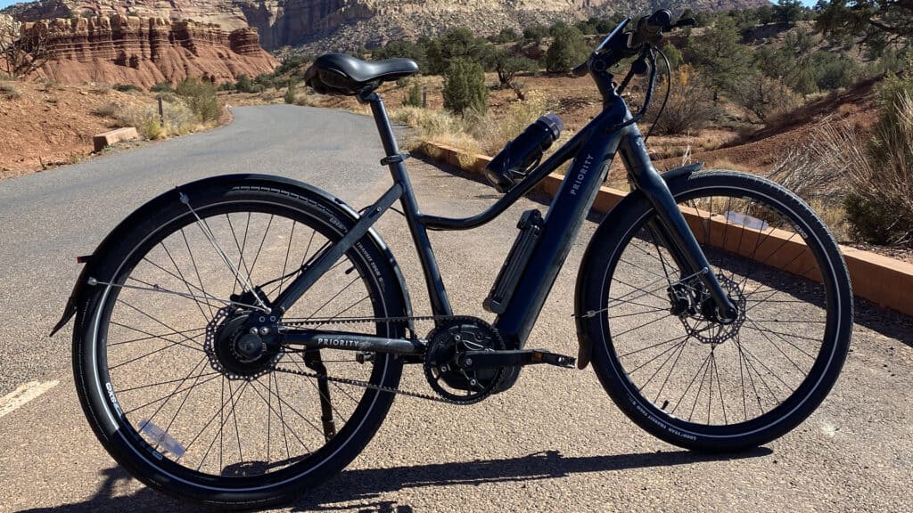 A side view of a Priority Current Belt Drive Electric Bike parked in the middle of rocky roads