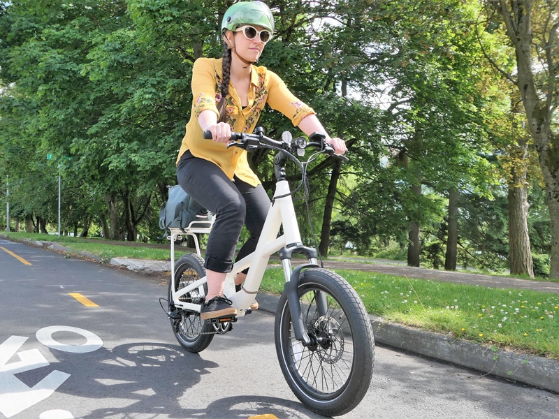 A view of a lady cycling the Co Op Cycles Generation E  electric bike on a road beside trees