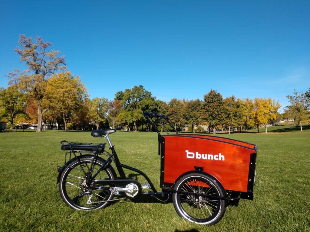 A view of a red Bunch Original Family Cargo Bike parked in a park