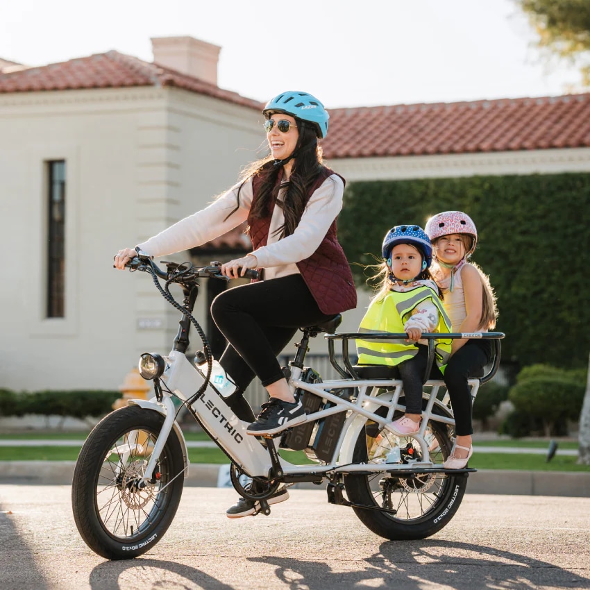 A view of a woman cycling a Lectric Xpedition Electric Cargo Bike with kids at the back