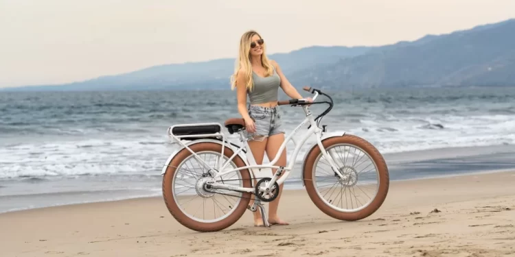 A girl standing with an e bike on a beach