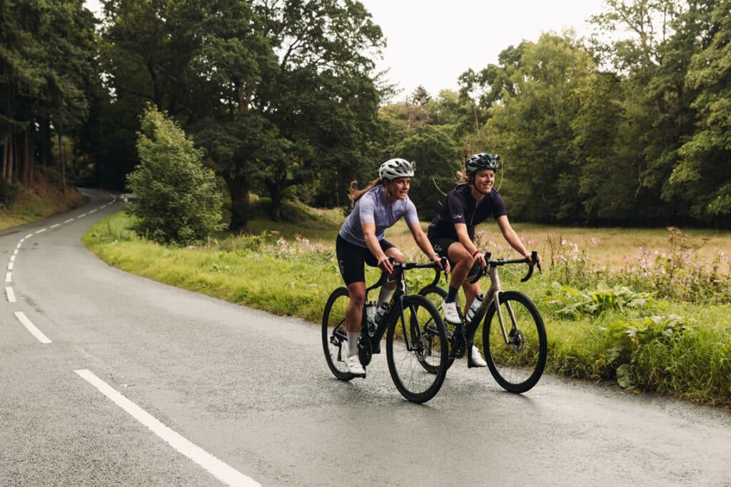 Two girls riding bike in a clean road by a field