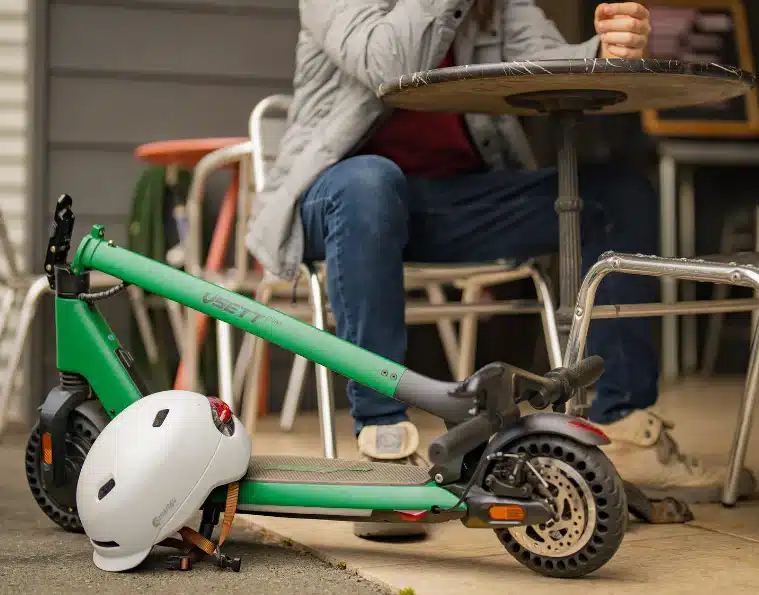 a foldable electric scooter with helmet and a man sitting on the chair behind