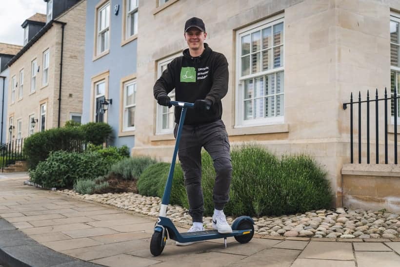 a man standing by holding his Unagi Model One Voyager electric scooter