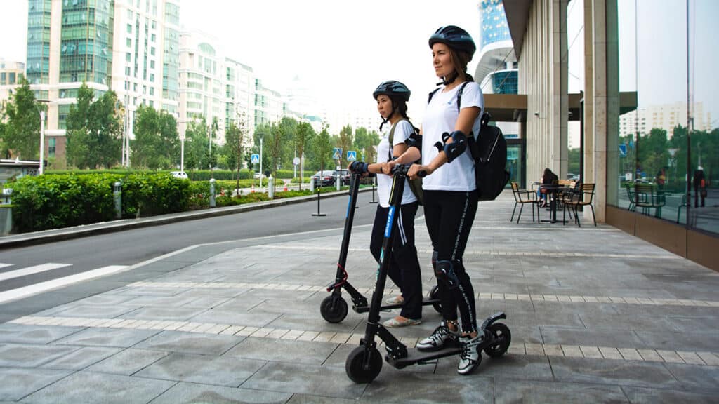 two girls standing by the road side on their electric scooters