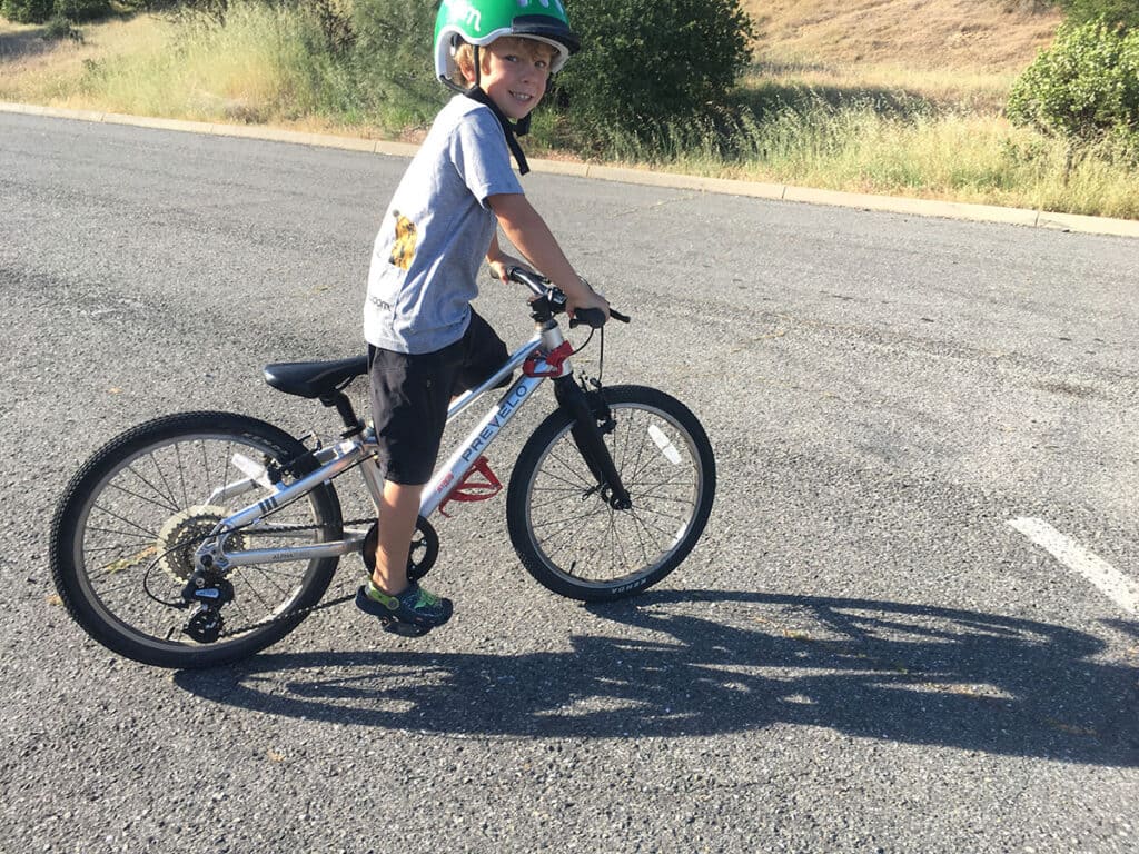 A view of a kid riding a bike with feet on pedal on a road