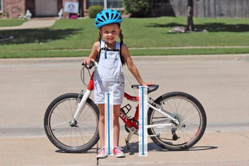 A view of a small girl standing beside a bike with height arrows mentioned for seat and inseam