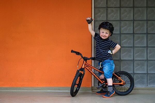 A view of a happy kid riding a bike waving one hand in air