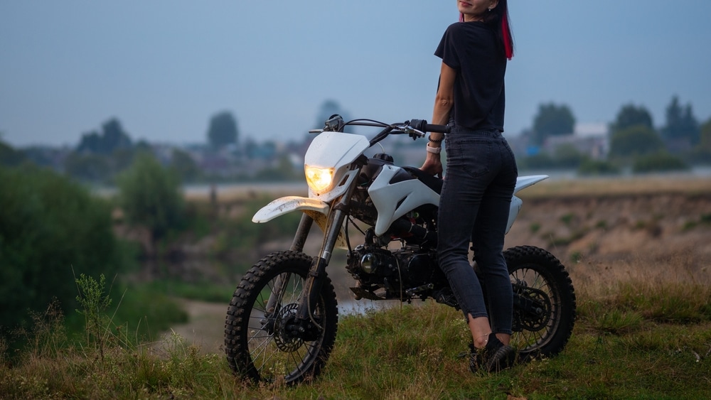 A view of a girl standing next to a pit bike in a field A view of a girl standing next to a pit bike in a field
